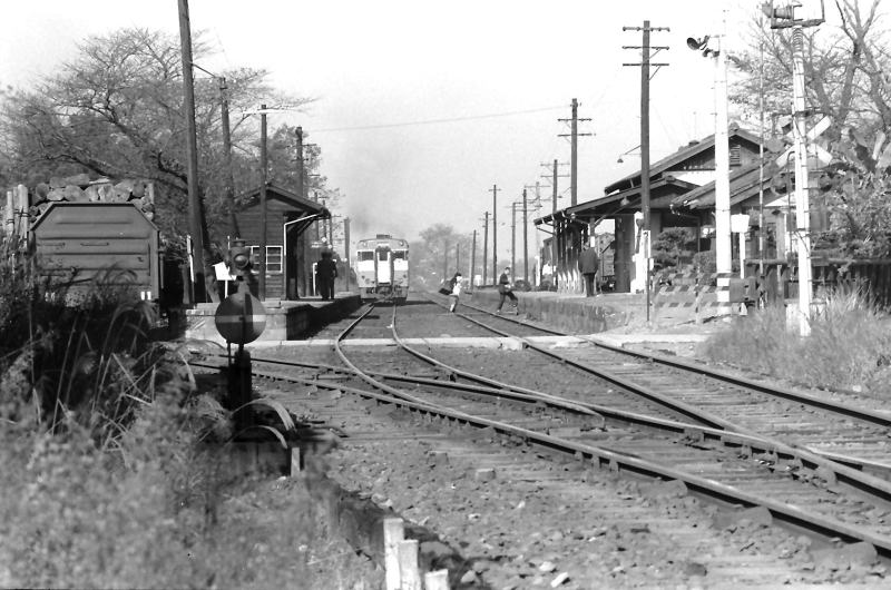 列車から降りて線路を渡る乗客と去っていく列車　見送る駅員。