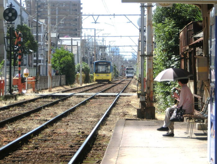 ベンチで日傘を差して電車を待つ