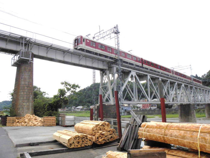 積まれた材木と、鉄橋を行く電車